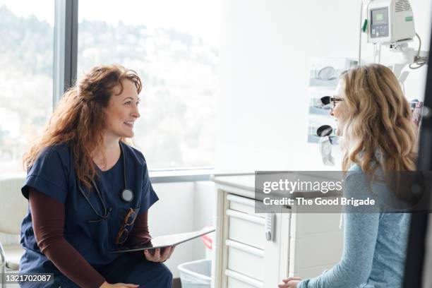 smiling nurse with digital tablet talking to teenage patient in medical clinic - patientin stock-fotos und bilder