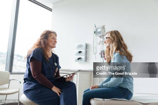 smiling female nurse using digital tablet while talking to teenage patient in clinic - caucasian doctor and nurse using tablet computer stock-fotos und bilder