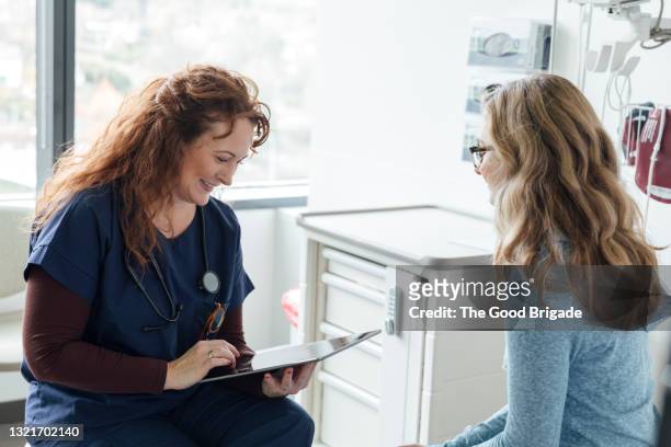 smiling female nurse using digital tablet while talking to teenage patient in clinic - healthcare tablet image focus technique stock pictures, royalty-free photos & images