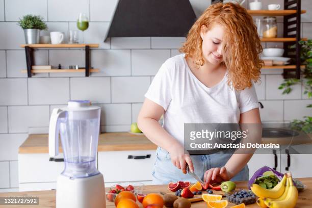 portrait of a beautiful smiling woman preparing smoothie at home kitchen. - fat people stock pictures, royalty-free photos & images