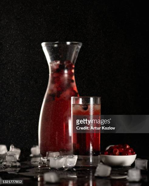 glass and jug of cherries beverage on table with frozen berries and ice cubes. wet glassware with red soft drink on black background with sprayed water drops. side view. soft focus. copy space - kirschen tisch weiß stock-fotos und bilder