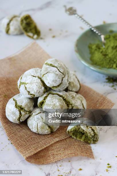 image of pile of freshly baked matcha tea amaretti cookies on piece of hessian beside plate of matcha tea with spoon, surrounded by crumbs and broken cookies, marble effect background, focus on foreground, elevated view - crack spoon stock pictures, royalty-free photos & images