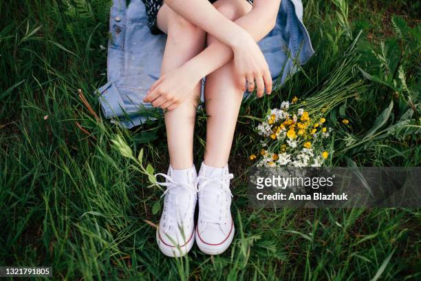 female legs in white sneakers. summer outdoors portrait of woman in green meadow of wild flowers. - scarpe di tela foto e immagini stock