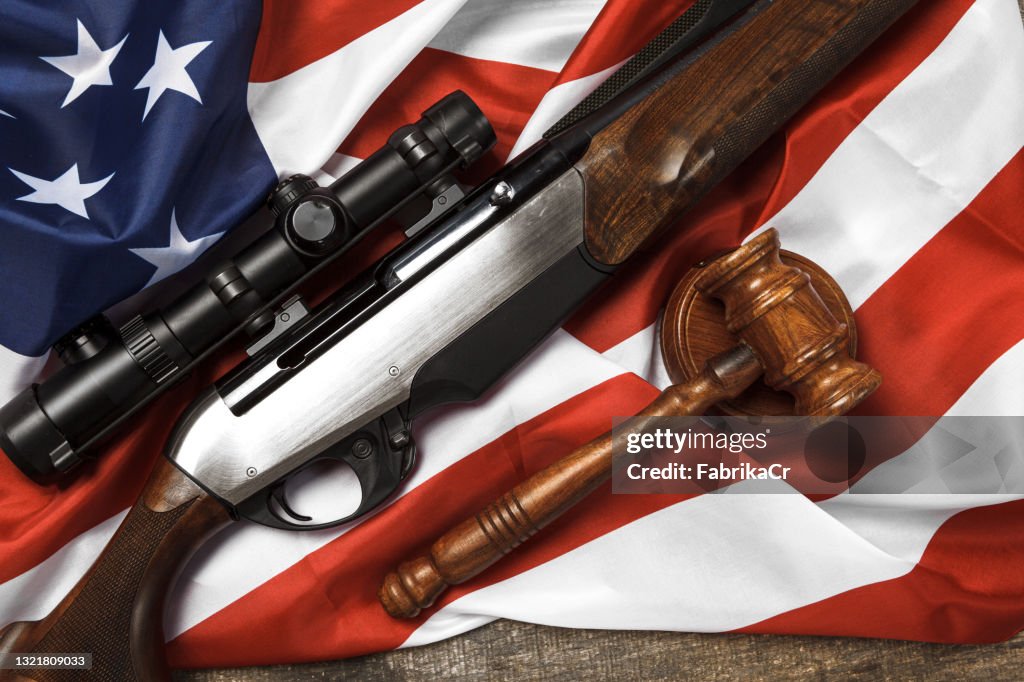 Wooden judge gavel and hunting rifle over USA flag on wooden background
