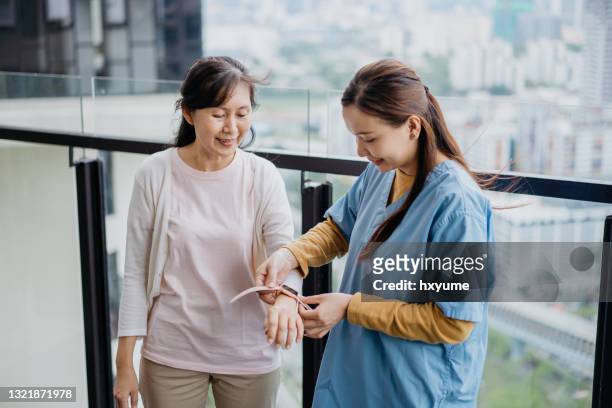 asian chinese caregiver wearing a smart watch on a patient's wrist - wearable technology stock pictures, royalty-free photos & images