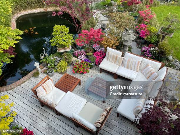 imagen de área de descanso al aire libre en terrazas soleadas de jardín de verano, cubierta de madera acanalada y encalada, asientos de madera dura con cojines, mesa de vidrio, estanque de peces de carpa koi, árboles bonsái, arces japoneses, jardín de - pond fotografías e imágenes de stock