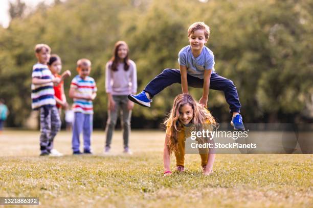 junge springt seine schwester auf der wiese - bockspringen stock-fotos und bilder
