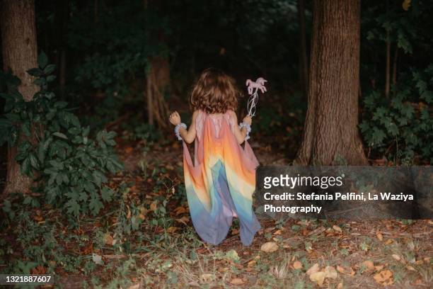 little girl in a silk rainbow fairy costume while walking in the woods - einhorn wald stock-fotos und bilder