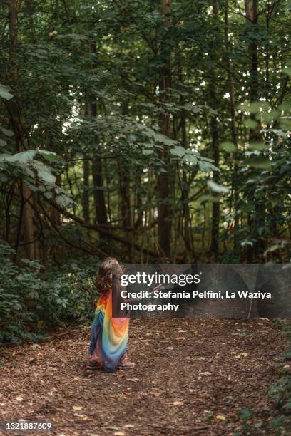 little girl in a silk rainbow fairy costume while walking in the woods - einhorn wald stock-fotos und bilder