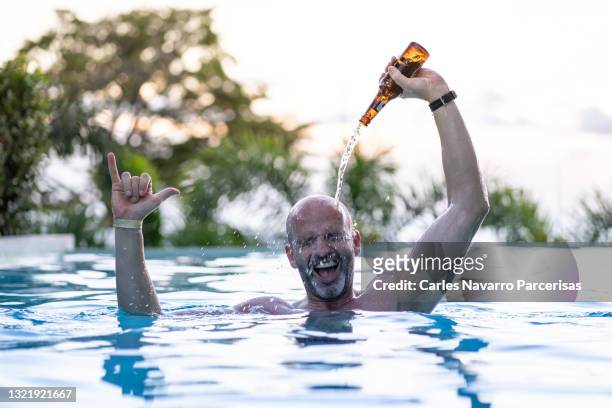 adult male in an outdoor swimming pool surrounded by nature throwing a beer on his head. - binge drinking stock pictures, royalty-free photos & images
