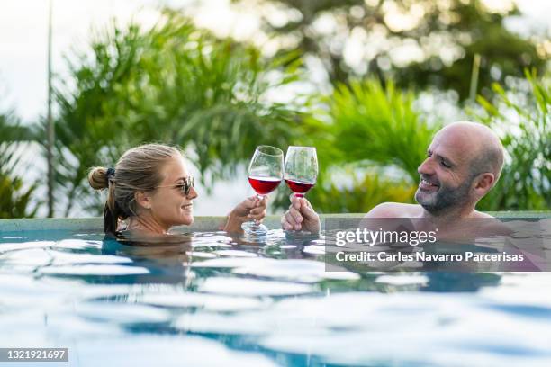 https://media.gettyimages.com/id/1321921697/photo/couple-toasting-into-a-outdoor-swimming-pool-surrounded-by-tropical-plants.jpg?s=612x612&w=gi&k=20&c=JcTMtct07J0K17_BzfMIDVuF_BLuvcOagSAJixSEJUo=