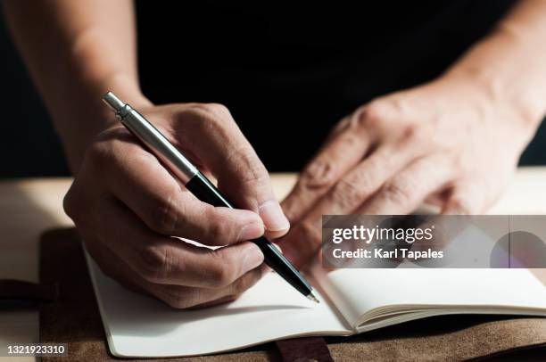 a close-up view of southeast asian man writing on a notepad - diary stockfoto's en -beelden