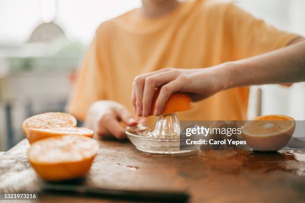 boy squeezing oranges to make juice at the kitchen - spremere foto e immagini stock