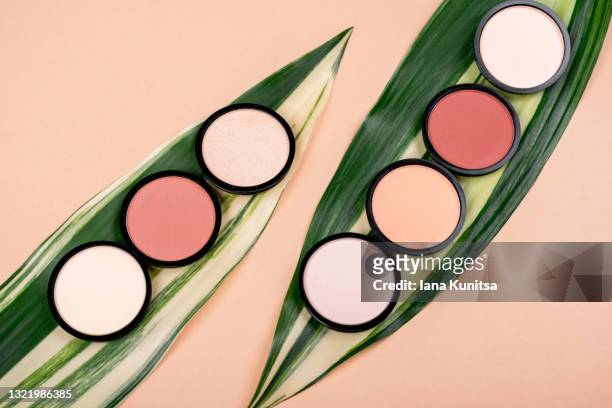 compact face powders, blush and eye shadow on beige background with green leaves. cosmetic products for makeup and skin care. - tipp ex stockfoto's en -beelden