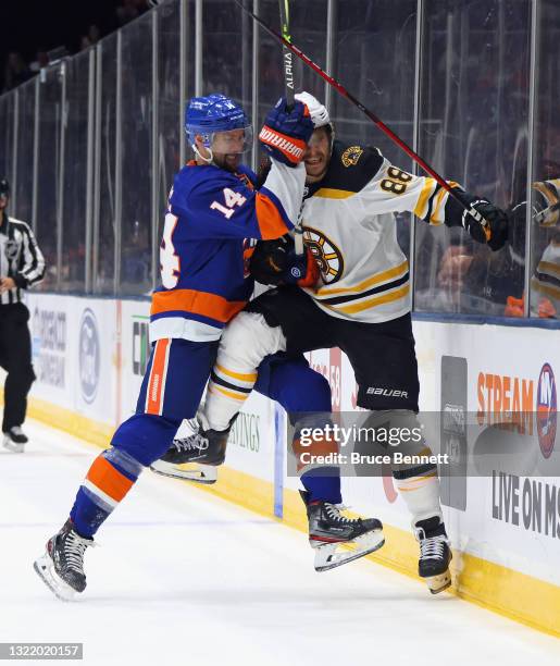 David Pastrnak of the Boston Bruins is checked into the boards by Travis Zajac of the New York Islanders during the first period in Game Four of the...