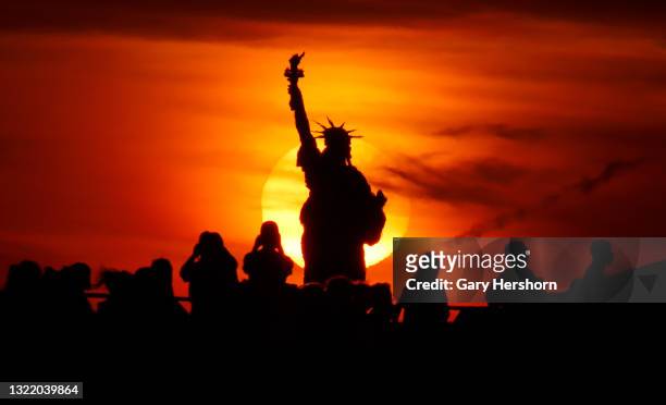 People watch from a ferry as the sun sets behind the Statue of Liberty on June 5, 2021 in New York City.