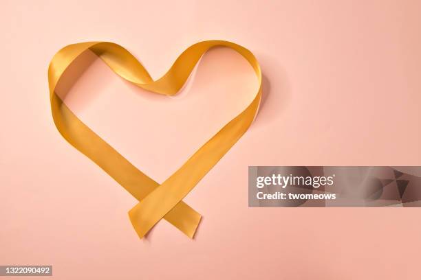 abstract heart shape form by satin ribbon on pink background. - gold satin ribon stock-fotos und bilder