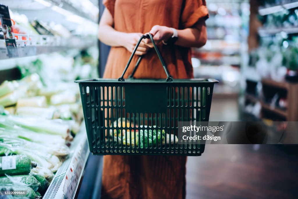 Cropped shot of young woman carrying a shopping basket, grocery shopping for fresh organic fruits and vegetables in supermarket. Green living. Healthy eating lifestyle