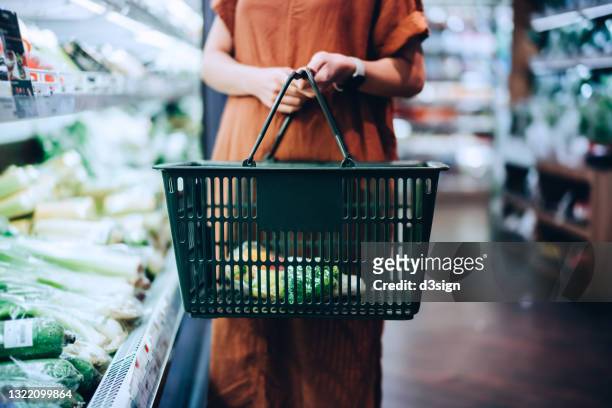 cropped shot of young woman carrying a shopping basket, grocery shopping for fresh organic fruits and vegetables in supermarket. green living. healthy eating lifestyle - shopping basket bildbanksfoton och bilder