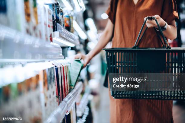 cropped shot of young woman carrying a shopping basket, standing along the product aisle, grocery shopping for daily necessities and buying fresh organic fruit juice from the shelf in supermarket - fruit juice stock pictures, royalty-free photos & images