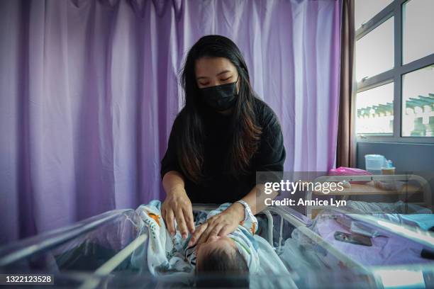 Gladys wearing a protective face mask as she swaddle her new born, Ezra in a nursery crib at a hospital on June 04, 2021 in Kuala Lumpur, Malaysia....