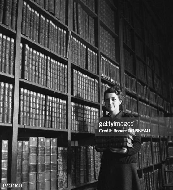 Une femme porte une pile de livres près des étagères, Bibliothe?que Nationale en 1942, Paris, France.