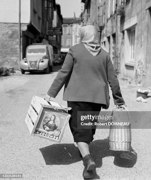 Une femme avec un foulard portant une caisse et un panier à Saint-Céré département du Lot, France.