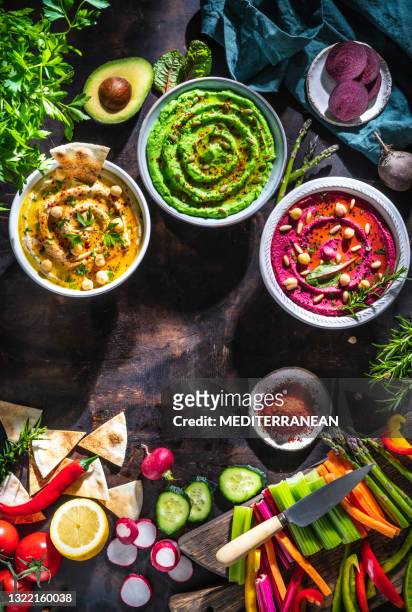 hummus tres bols de garbanzos, aguacate y remolacha con verduras cortadas pegados sobre mesa de madera oscura - vegan food fotografías e imágenes de stock