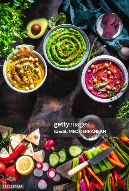 hummus drie kom kikkererwten, avocado en rode biet met besnoeiingsgroentenstokken op donkere houten lijst - mediterranean food stockfoto's en -beelden