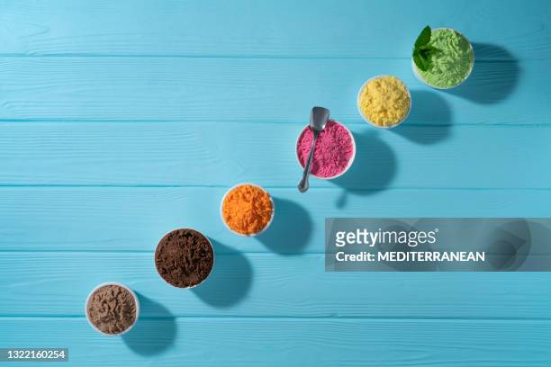 tazas de helado variadas en una fila y conos de gofres coloridos sobre fondo de madera azul - ice cream cup fotografías e imágenes de stock
