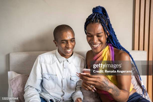afroamerikansk icke-binär person och transsexuell kvinna i sängen med smart telefon och prata. hbtq-par. - transgender bildbanksfoton och bilder