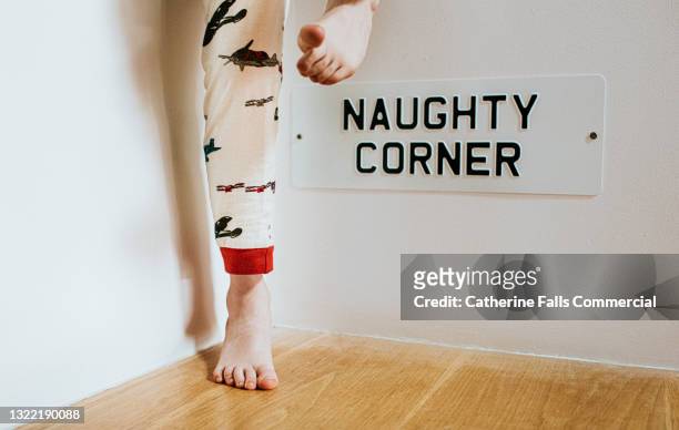 naughty corner - a tin sign mounted on a wall displays a comical message as a child in pyjamas stands beside it - childish stock pictures, royalty-free photos & images