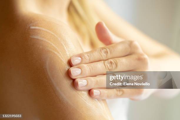 body skin care after the shower, a young woman applies a moisturizing lotion on her shoulder.  female beauty routine - douche savon photos et images de collection