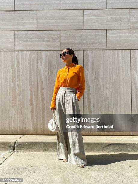 Julia Comil wears a bright orange silk blouse with white piping detail, long sleeves by Equipment, beige linen high waisted wide trousers oversized...