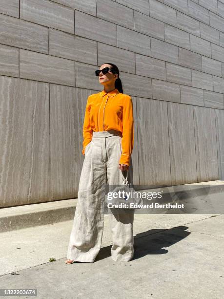 Julia Comil wears a bright orange silk blouse with white piping detail, long sleeves by Equipment, beige linen high waisted wide trousers oversized...