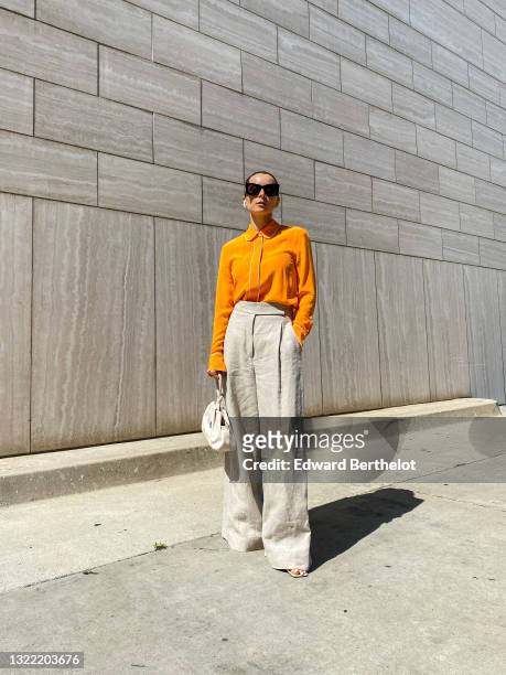 Julia Comil wears a bright orange silk blouse with white piping detail, long sleeves by Equipment, beige linen high waisted wide trousers oversized...