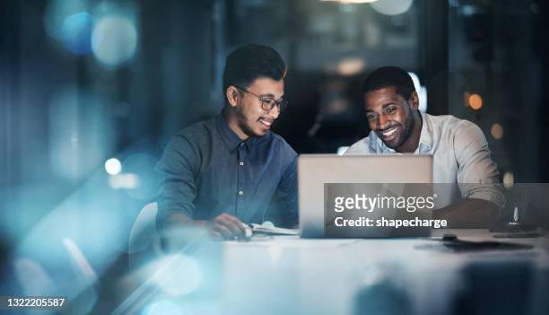 tiro cortado de dois jovens empresários trabalhando juntos em um laptop em seu escritório tarde da noite - enterprise - fotografias e filmes do acervo