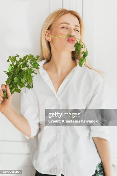 young woman making funny face, holding a parsley mustache. - funny vegetable stock-fotos und bilder