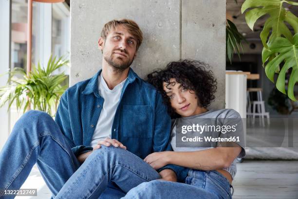 tired couple leaning on column while sitting on floor at home apartment - boyfriend stockfoto's en -beelden