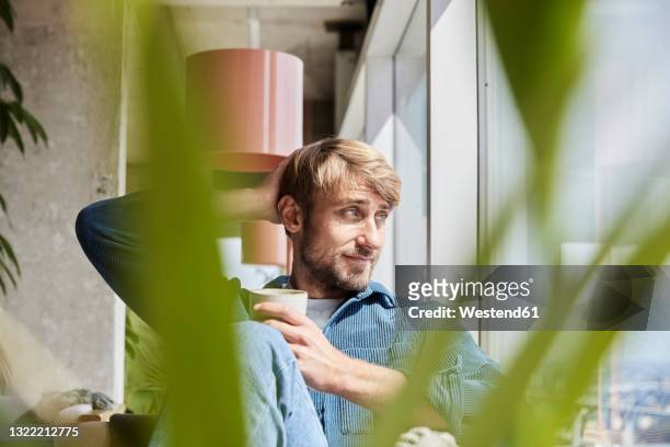 handsome man with hand in hair looking away while sitting at loft - solo un uomo di età media foto e immagini stock