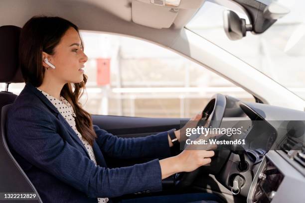 businesswoman driving car while wearing in-ear headphones - car interior side stock pictures, royalty-free photos & images