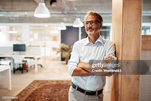 smiling male entrepreneur looking away while leaning on wall - 60 64 ans photos et images de collection