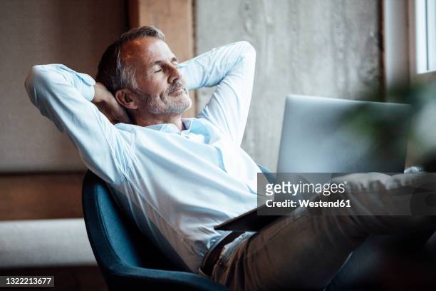 senior male entrepreneur sitting with laptop on chair - hands behind head stock pictures, royalty-free photos & images