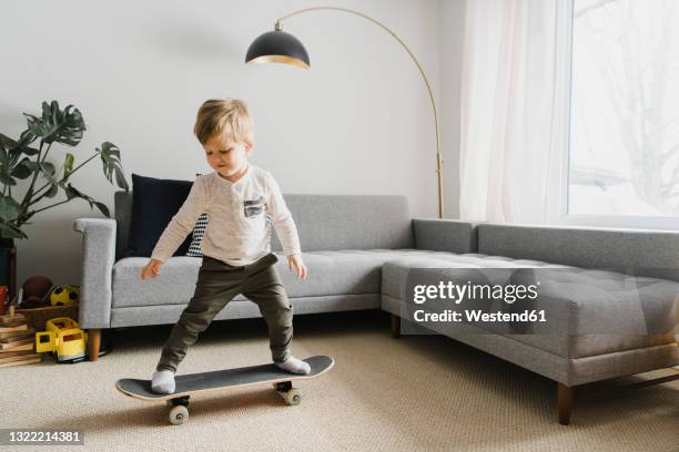 toddler boy skateboarding in living room at home - indoor skating stock pictures, royalty-free photos & images
