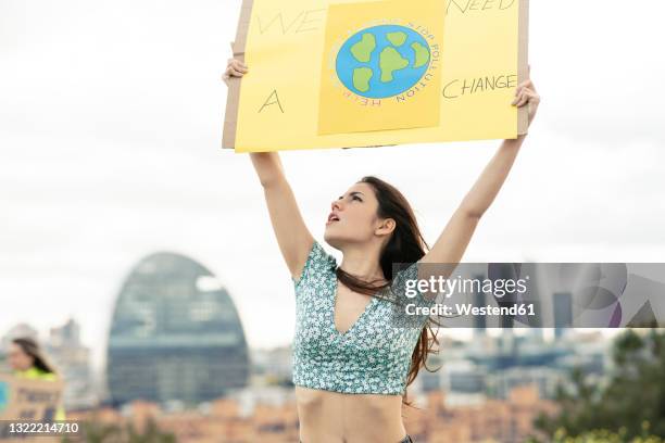young woman looking up while holding banner below sky - ambientalista foto e immagini stock