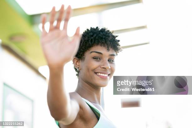 smiling young woman waving outdoors - curly waves stock pictures, royalty-free photos & images