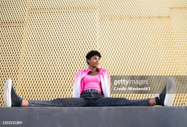 young woman looking away while sitting with spreading legs by wall - woman leg spread stock pictures, royalty-free photos & images