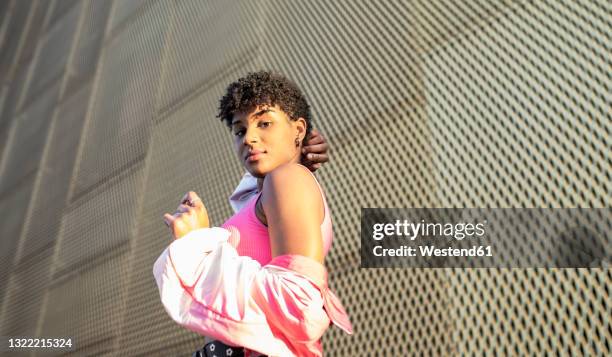 young woman near wall during sunny day - off the shoulder coat stock pictures, royalty-free photos & images