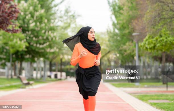 beautiful woman in headscarf looking away while running in public park - voile religieux photos et images de collection