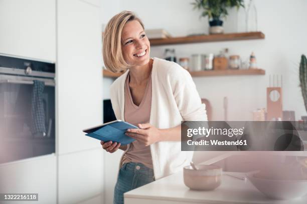 smiling woman looking away while leaning on kitchen counter at home - kitchen front view stock pictures, royalty-free photos & images